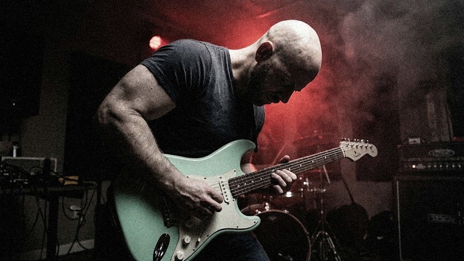 Pete leaning into an electric guitar under red stage light and haze
